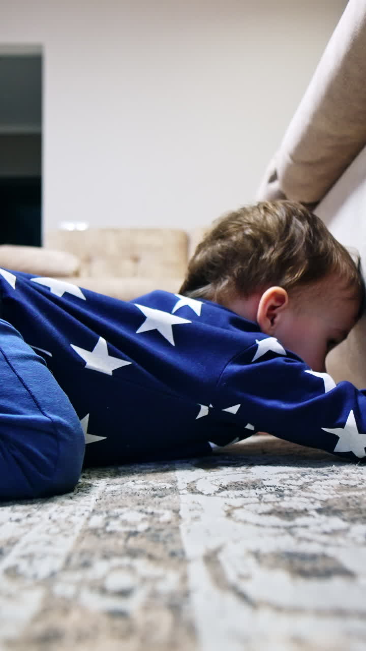 Funny little kid wants to get something from under the sofa. Boy shoves his hand under the furniture but can't get what he wants. Vertical video