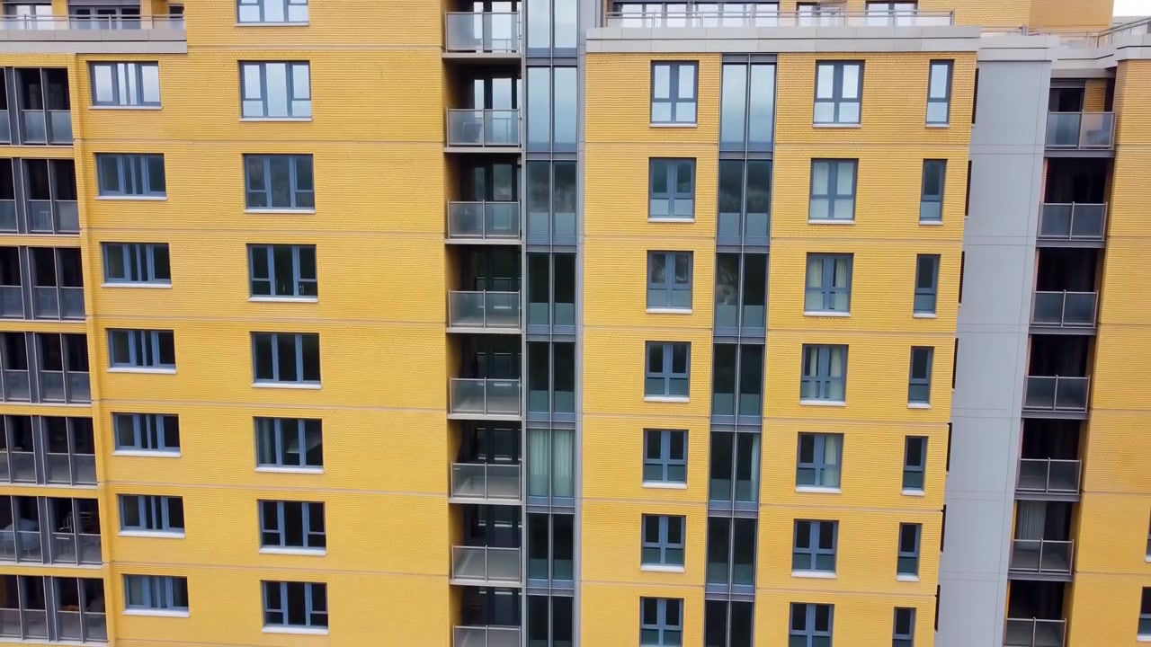 Inspección con dron de fachada de edificio de apartamentos amarillo, torre residencial moderna con hueco de ascensor de cristal, filas.
