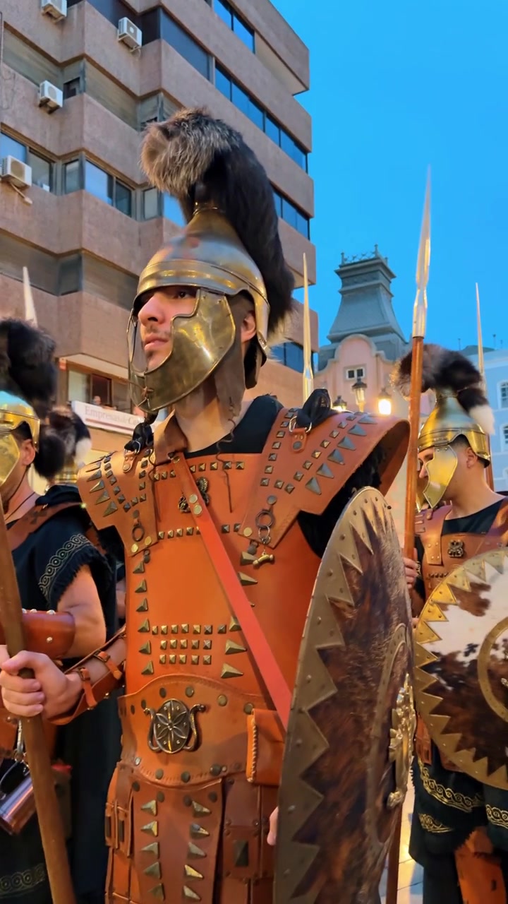 Alicante, Hiszpania, 8 sierpnia 2025: Rekonstruktor w rzymskiej zbroi oficerskiej i hełmie podczas parady ulicznej. Zbliżenie mężczyzny w skórzanym napierśniku i hełmie z grzebieniem, trzymającego włócznię podczas wieczornego wydarzenia.