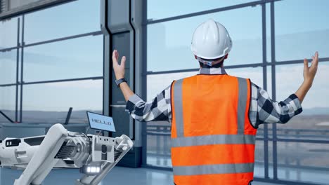 vista trasera de un ingeniero asiático con casco de seguridad extendiendo los brazos mientras está de pie en una fábrica de alta tecnología, analizando el concepto de máquina robótica