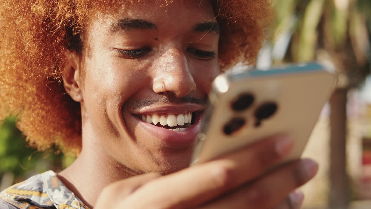 Giovane uomo con capelli rossi ricci che sorride e parla allo smartphone