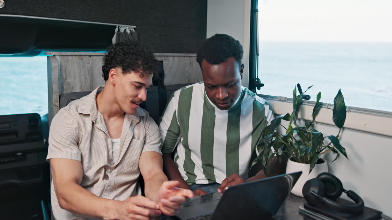 Two Young Men Collaborating on Laptop Inside a Camper Van