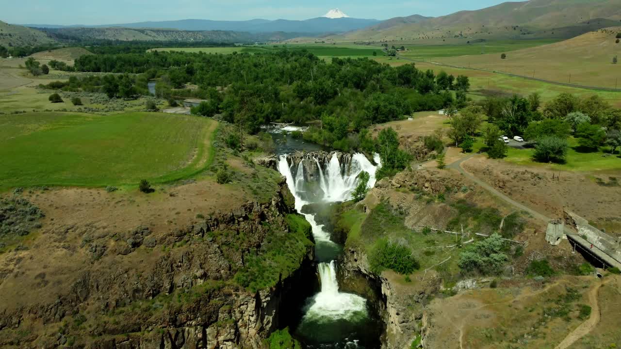 US, Oregon, Tygh Valley, White River Falls, 2025-05-09 - Drone view of the White River Falls in north central Oregon in the spring with Mt Hood covered in snow in the distance