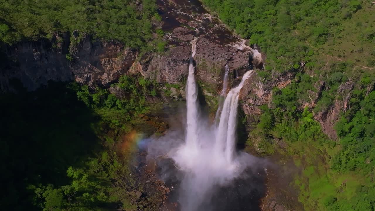 Cachoeira dos Saltos waterfall is creating a rainbow while plunging into a rocky pool surrounded by lush vegetation in Chapada dos Veadeiros National Park, a UNESCO World Heritage site in Brazil