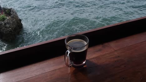 cup of brewed black coffee on wooden platform by the sea