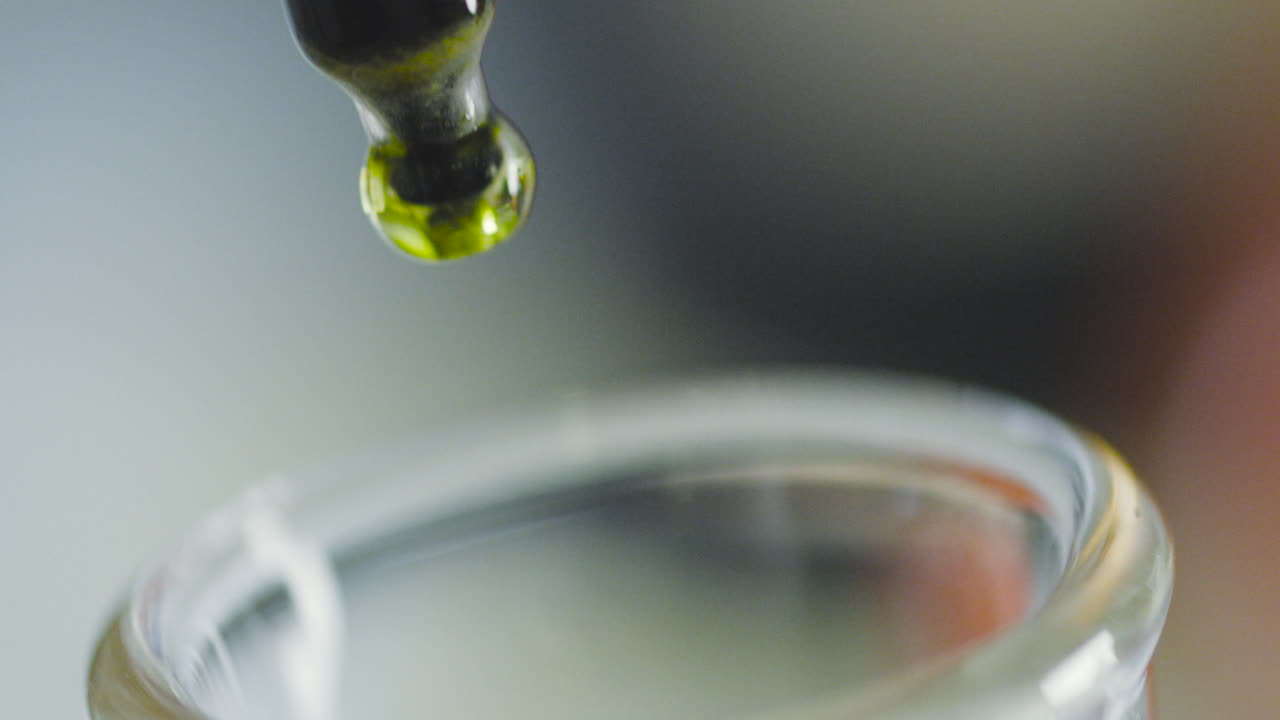 Close-up capturing the moment a drop of colored liquid falls from a test tube into a beaker.