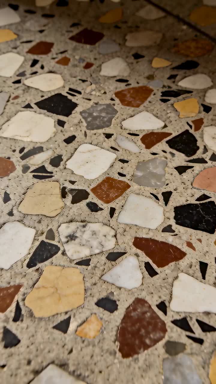 Video vertical: Cámara moviéndose y revelando un suelo de terrazo en un pasillo, mostrando coloridas incrustaciones de piedra.
