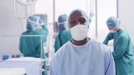 video portrait of african american male surgeon in mask smiling in operating theatre, copy space