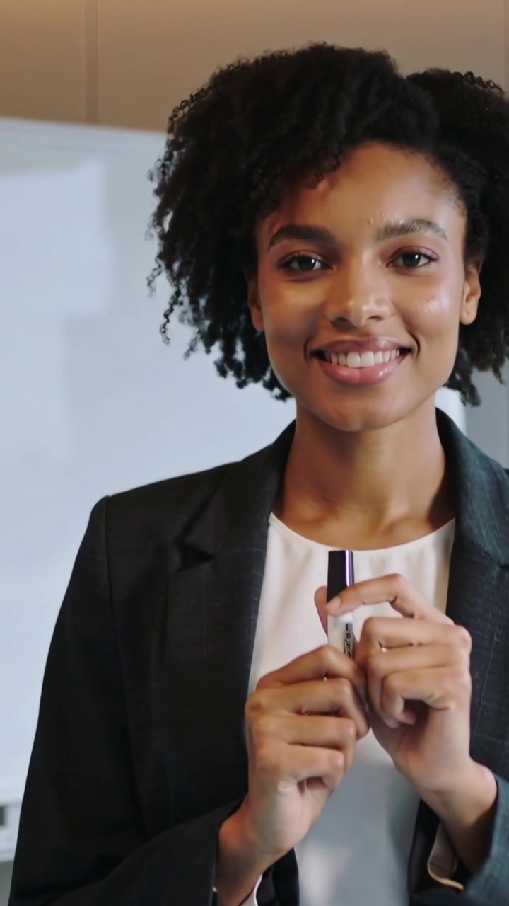 Vertical video: Smiling teacher holding marker at whiteboard as camera zooms, preparing in blazer