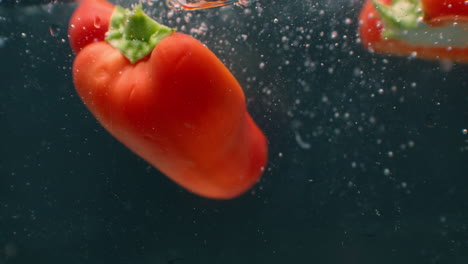 close up several cut slices of fresh green and red bell pepper thrown and floating in clear transparent water low angle side view slow motion