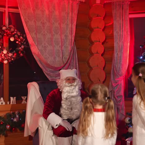 santa claus and kids in the house. happy santa with white beard sits into armchair and listen to children. christmas decorated room background