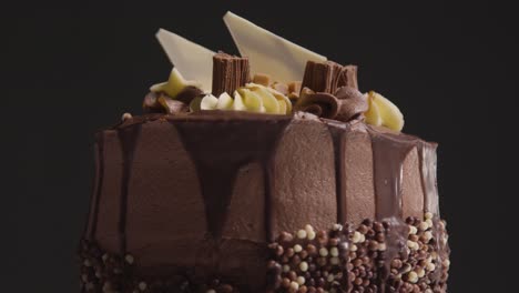 close up studio shot of freshly baked and decorated chocolate celebration cake revolving against black background