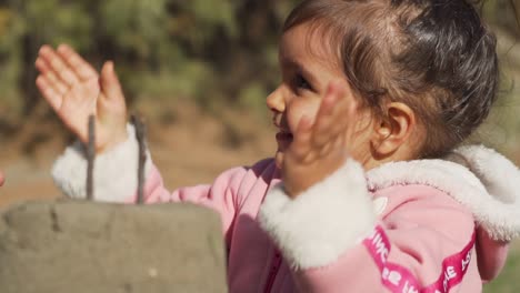 linda niña aplaudiendo y cantando feliz cumpleaños en un pastel de arena en la playa