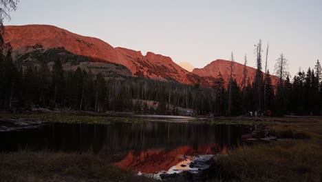 landscape tilting up shot of the beautiful butterfly lake surrounded by large rocky mountains and pine trees inside of the uinta wasatch cache national forest in utah during a warm summer sunset