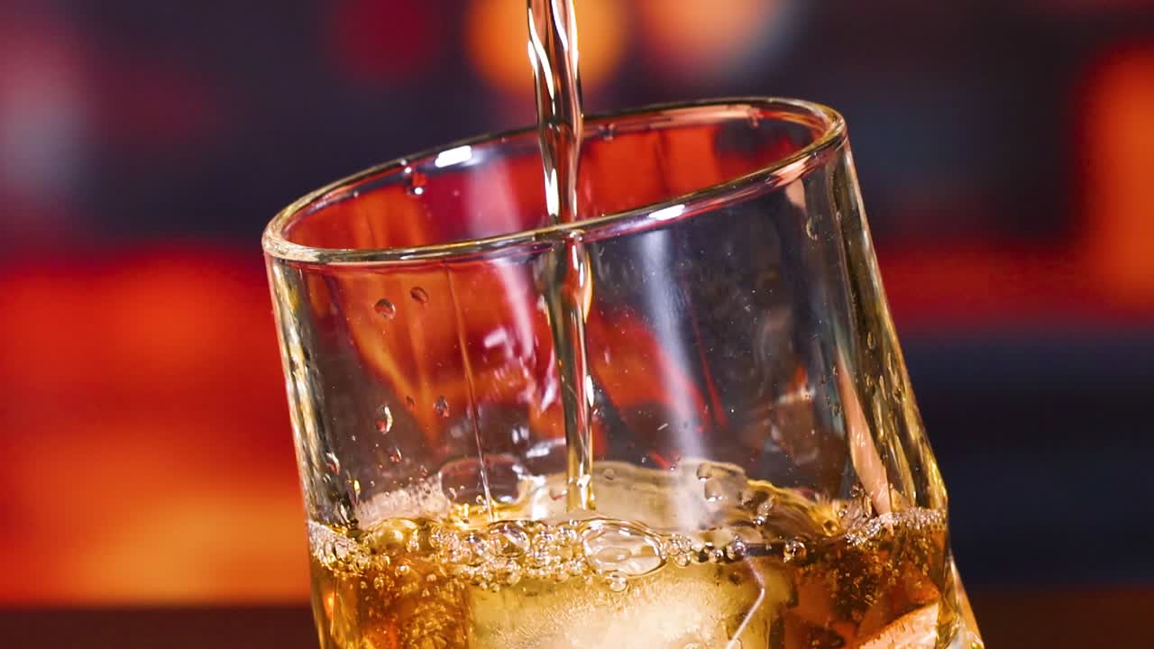 Close-up of amber liquid being poured into a glass with ice cubes, creating a refreshing beverage.
