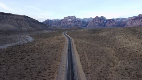 Aerial-crane-shot-of-cars-driving-towards-the-camera-and-away-from-Red-Rock-Canyon-at-sunrise