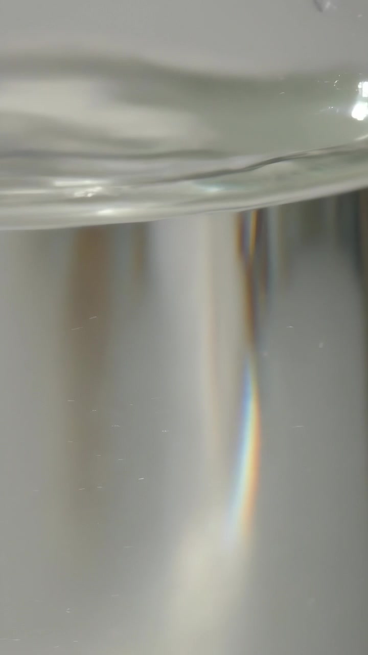 Video verticale: Telecamera in movimento che mostra il bordo di un bicchiere e l'acqua che forma increspature sulla scrivania, banda prismatica in movimento.