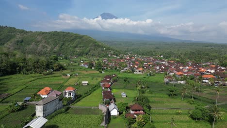 drone flying over rice terrace farm land and a small village with a volcano in the background