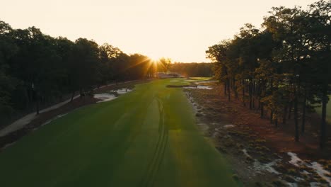 aerial drone shot down shot moving down the fairway of a golf course as the rising sun peaks over the trees