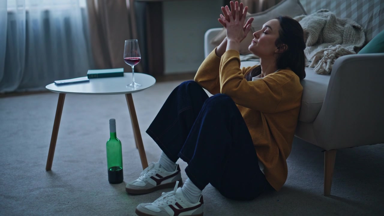 Troubled woman sitting floor leaning on couch with wine bottle and glass
