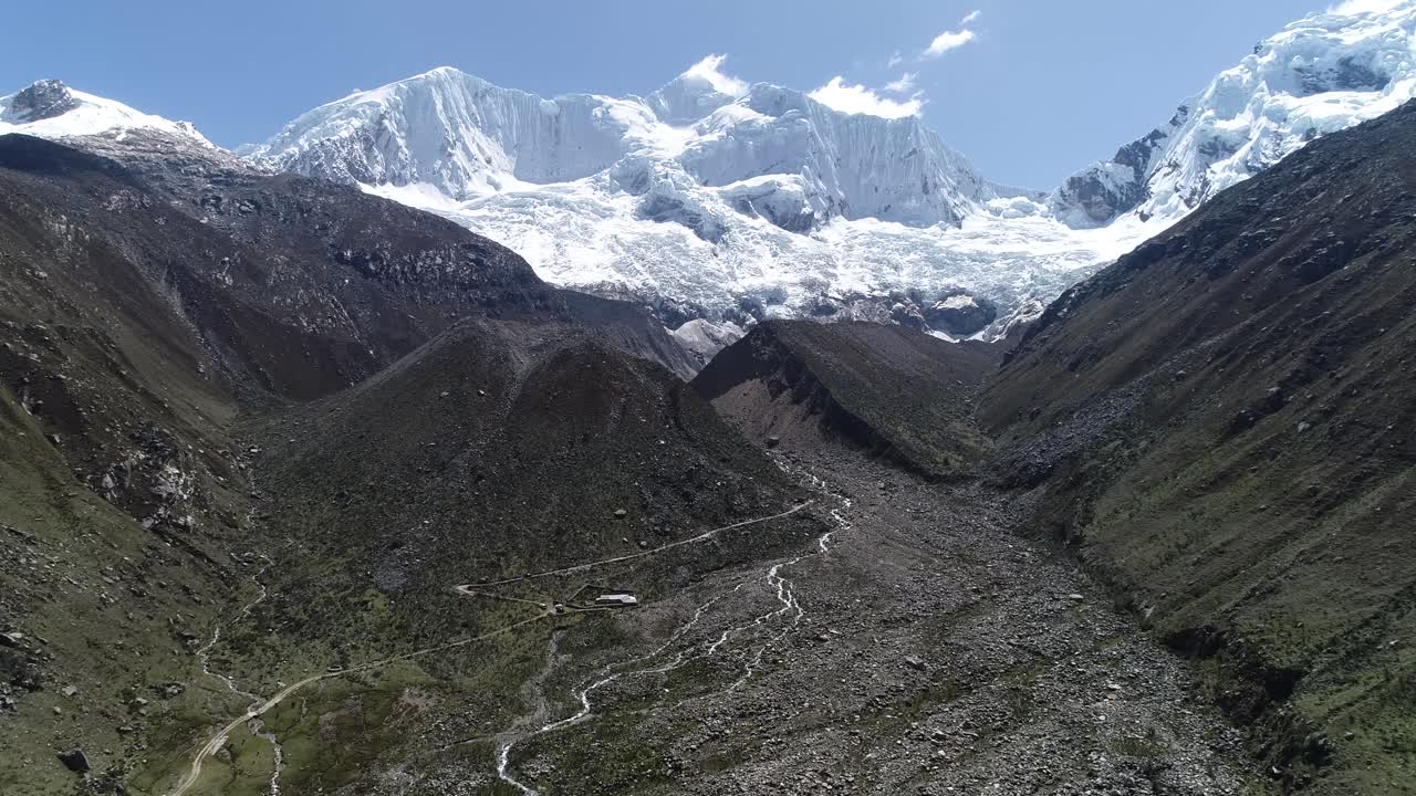 A breathtaking glacier towers over a rocky Andean valley, with a winding stream carving through the rugged terrain. Ideal for travel, nature, and environmental projects
