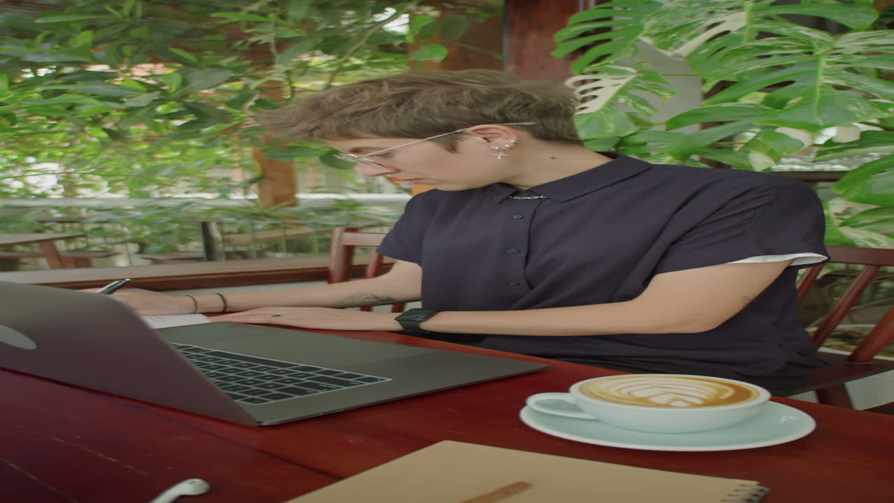 Woman Working on Laptop and Taking Notes in Outdoor Summer Cafe