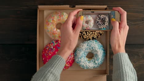 woman's hands take pictures with smartphone of delicious donuts in box