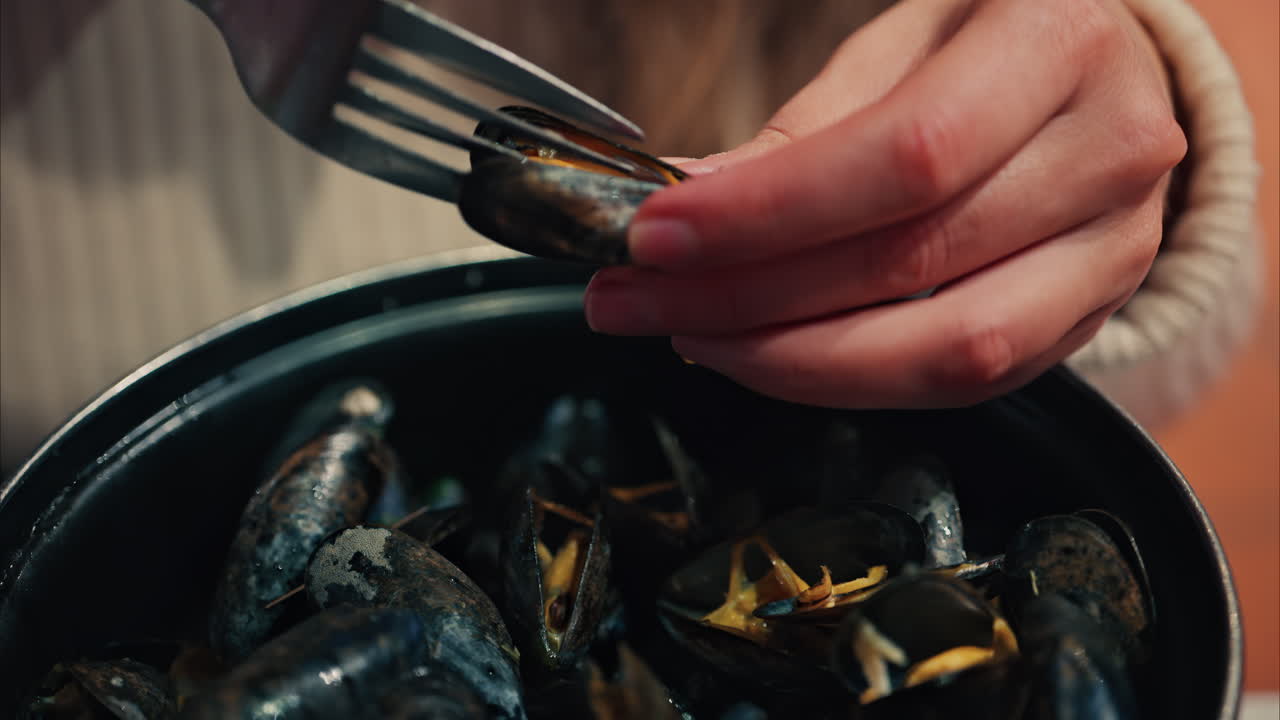 Close up of a woman eating mussels from a pan with a fork