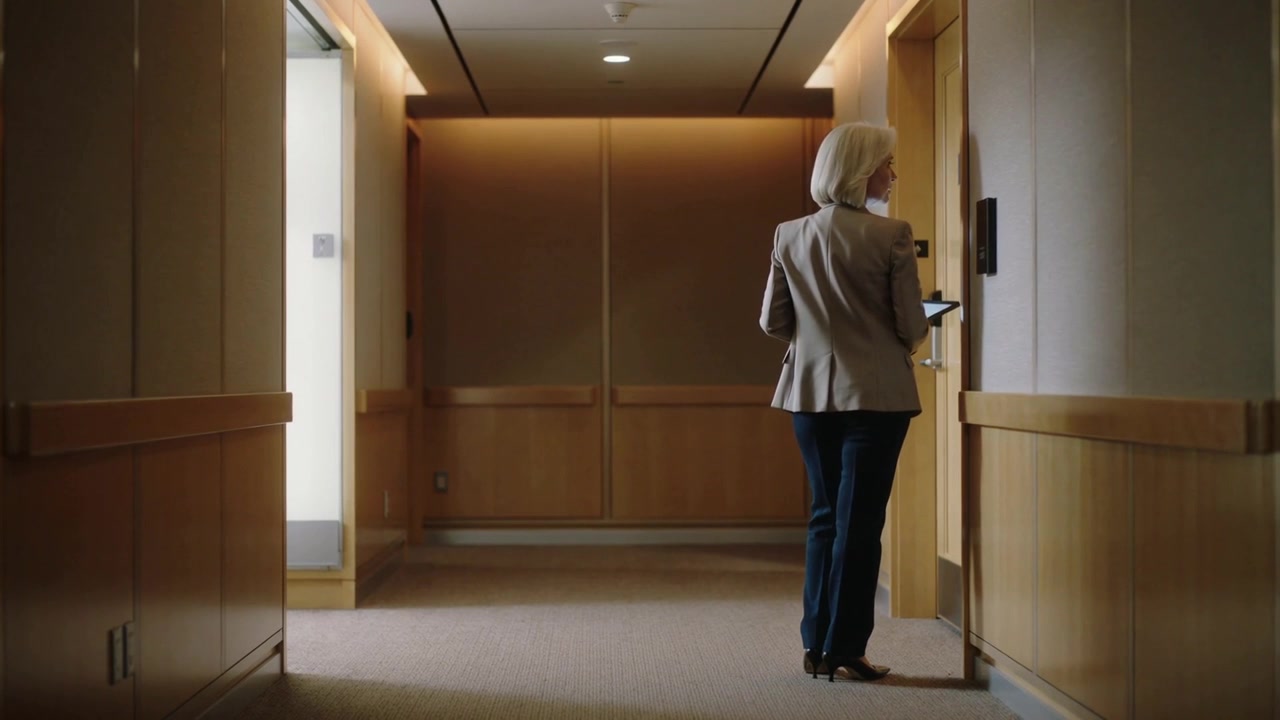 Walking senior woman in blazer with tablet at door, using access panel to enter office hallway