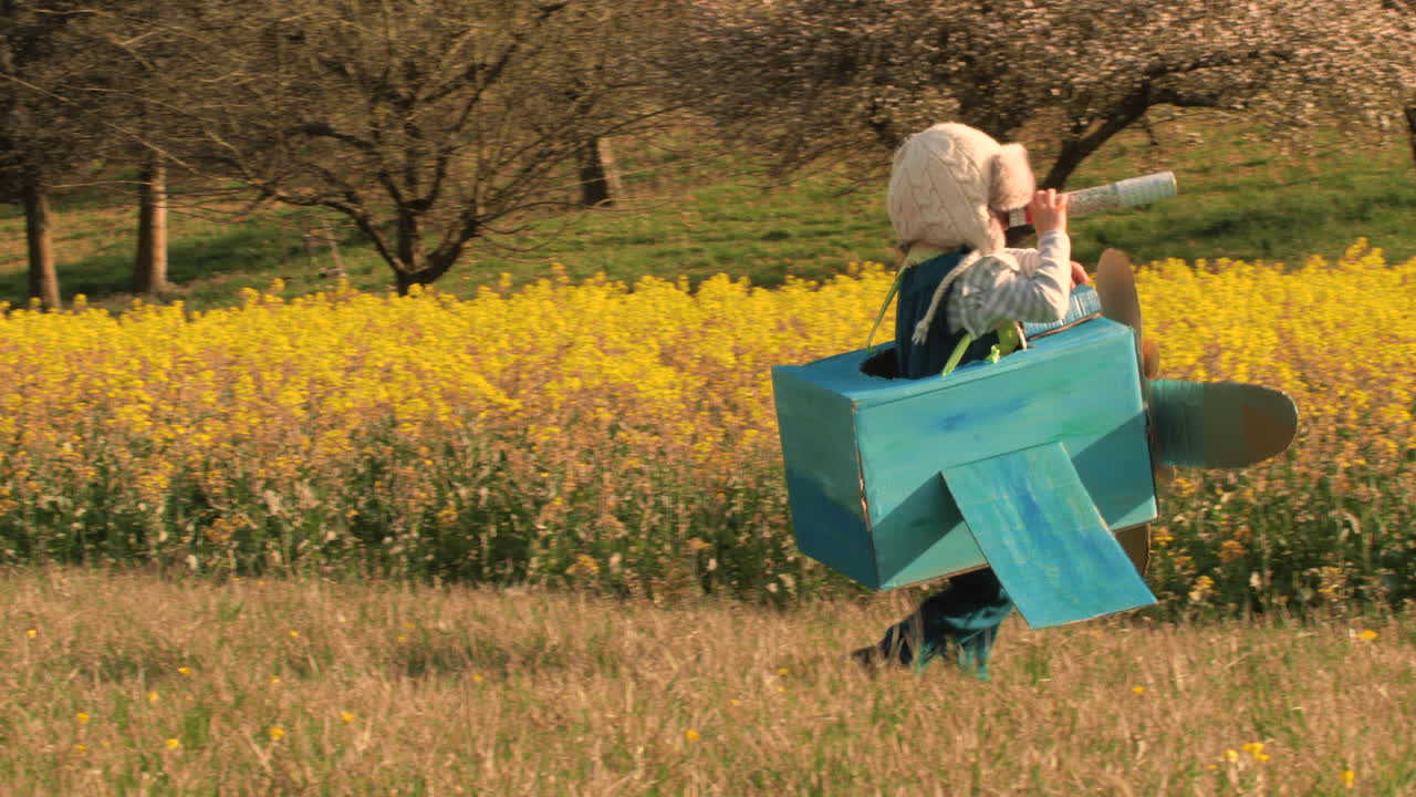Happy child runs with a toy airplane over a field during sunset. Little Kid pretend to fly as a pilot in the sky with paper airplane. The concept of a happy family, freedom, childhood and dreams.