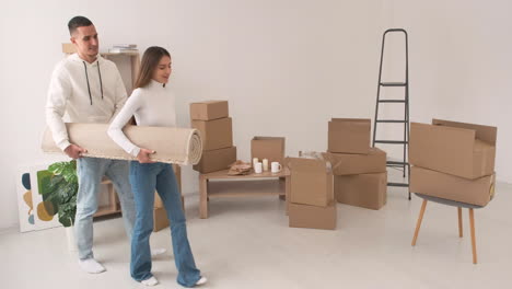 young couple carrying a big carpet in a new house