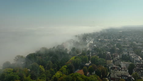 aerial shot of sopot shrouded in fog, with lush trees and urban buildings emerging through the misty landscape.