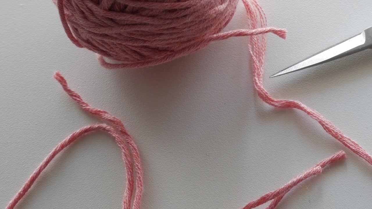 Close-up of pink yarn ball and scissors on table under daylight, representing cozy autumn craft activity