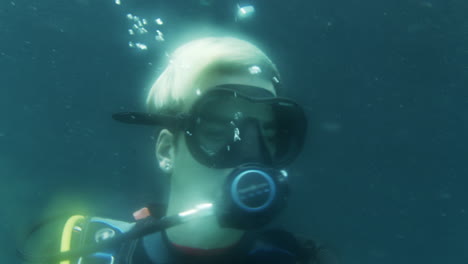 adulto joven en traje de buceo mirando y girando, atmósfera de ensueño, cabello rubio