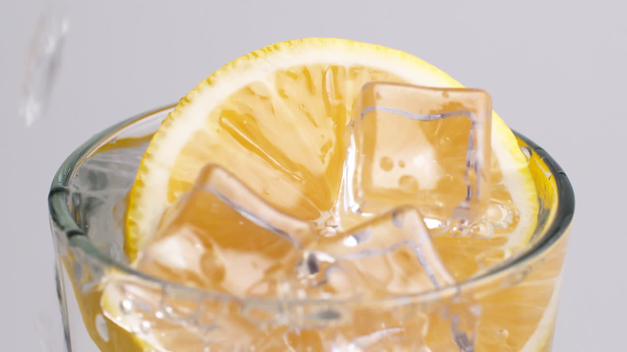 Acqua fredda frizzante fresca che si versa in un bicchiere con ghiaccio e fette di limone-2