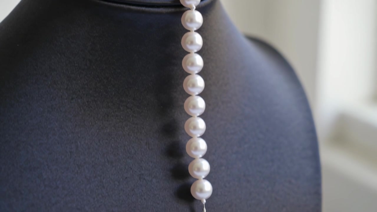 Collana di perle bianche che scivola lungo un espositore imbottito nero su un tavolo, con la gravità che tira il filo
