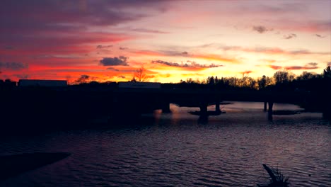 Coches-Cruzando-El-Puente-Del-Río-Con-Una-Hermosa-Puesta-De-Sol-En-El-Fondo