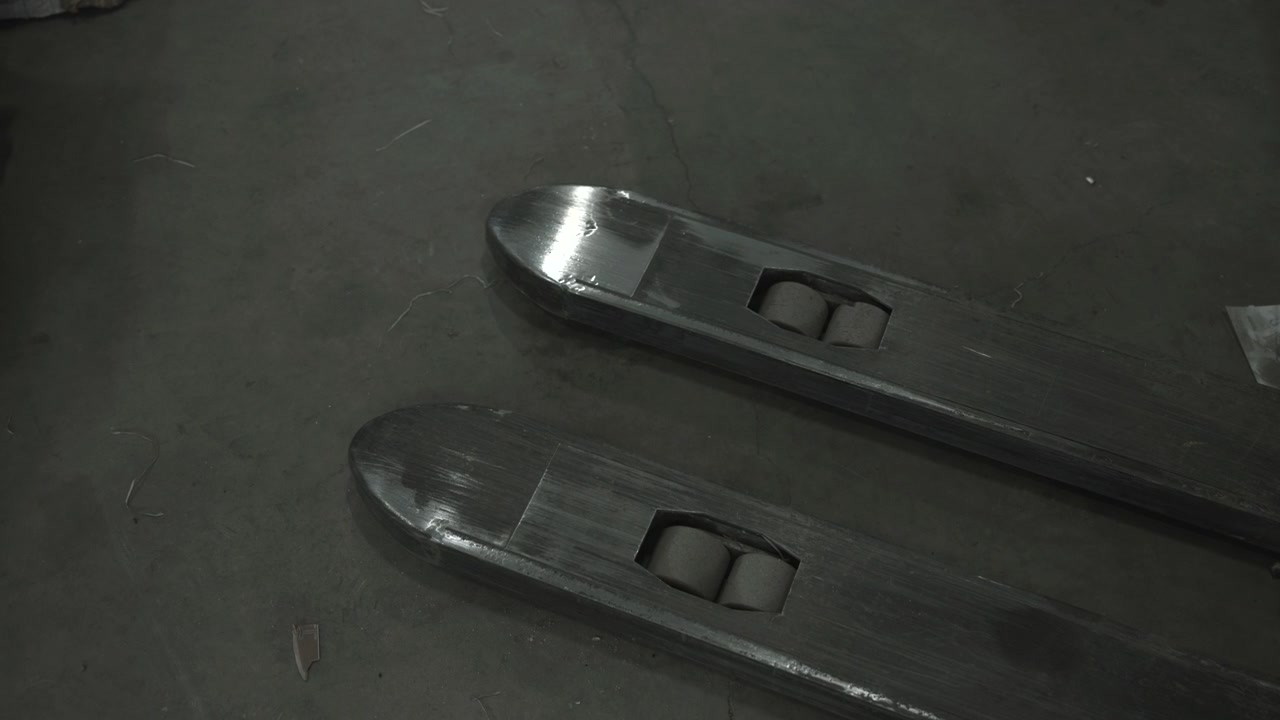 Primo piano delle forche del transpallet su pavimento in cemento, rulli usurati e denti metallici, attrezzatura inattiva in una baia di carico buia
