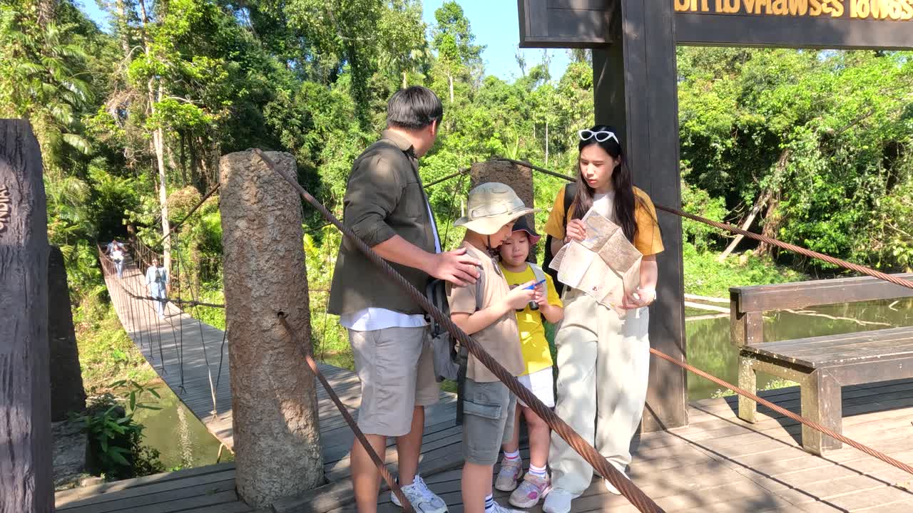 Uma família de quatro pessoas está em pé em uma ponte de madeira em Khao Yai, consultando um mapa.