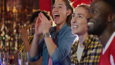 video of diverse group of happy friends drinking and watching sports game at a bar, celebrating