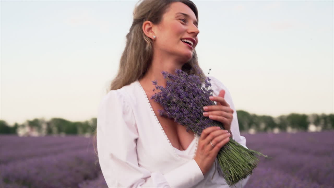 Woman in a white dress smelling a bouquet of lavender in a field