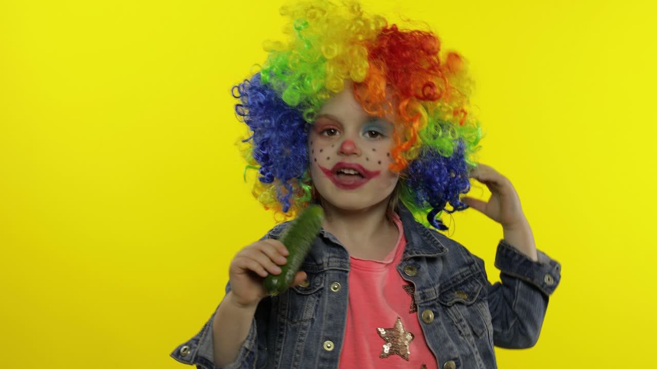 una pequeña niña payasa con una peluca colorida haciendo caras tontas, cantando, sonriendo, bailando. halloween
