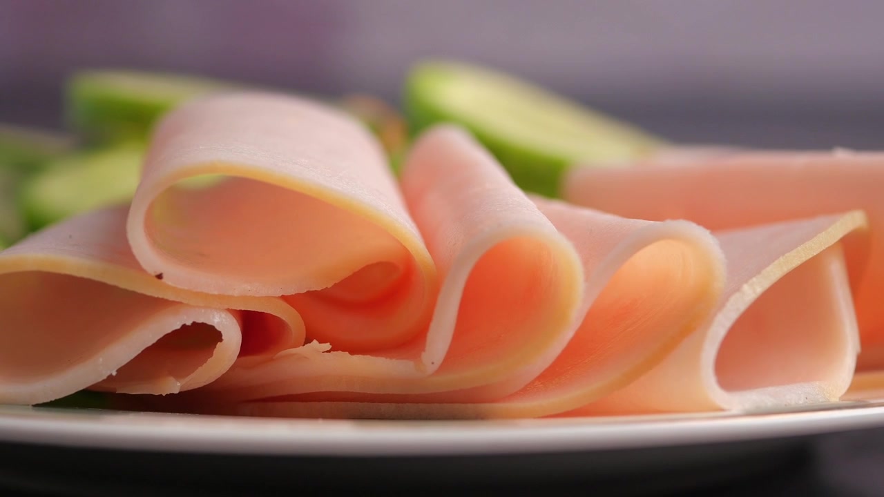 Primo piano di prosciutto affettato e cetriolo su un piatto bianco