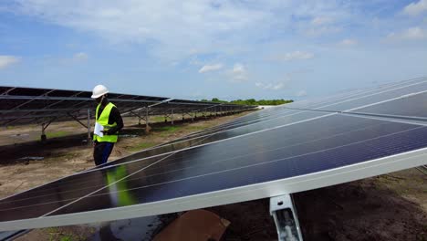 Schwarzer-Männlicher-Afrikanischer-Ingenieur,-Der-Mit-Schutzhelm-In-Einem-Solarpanel-Bauernhof-Für-Erneuerbare-Energien-Spaziert-Und-Ein-Papiernotizbuch-Mit-Messdaten-Zur-Effizienz-Von-Photovoltaikanlagen-In-Afrika-Trägt