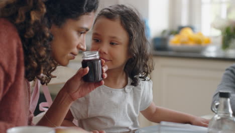 Familia-Feliz-Desayunando-Juntos-Niña-Curiosa-Haciendo-Preguntas-Aprendiendo-Con-La-Madre-Enseñando-A-Su-Hija-Disfrutando-De-Un-Delicioso-Manjar-En-La-Cocina-De-Casa