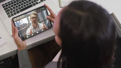 biracial businesswoman using tablet for video call with caucasian business colleague