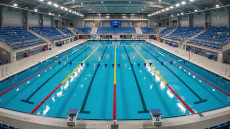 an expansive view of a modern indoor swimming pool with six lanes, vivid blue water, red lane markers, and ample spectator seating, ready for competitions and training sessions