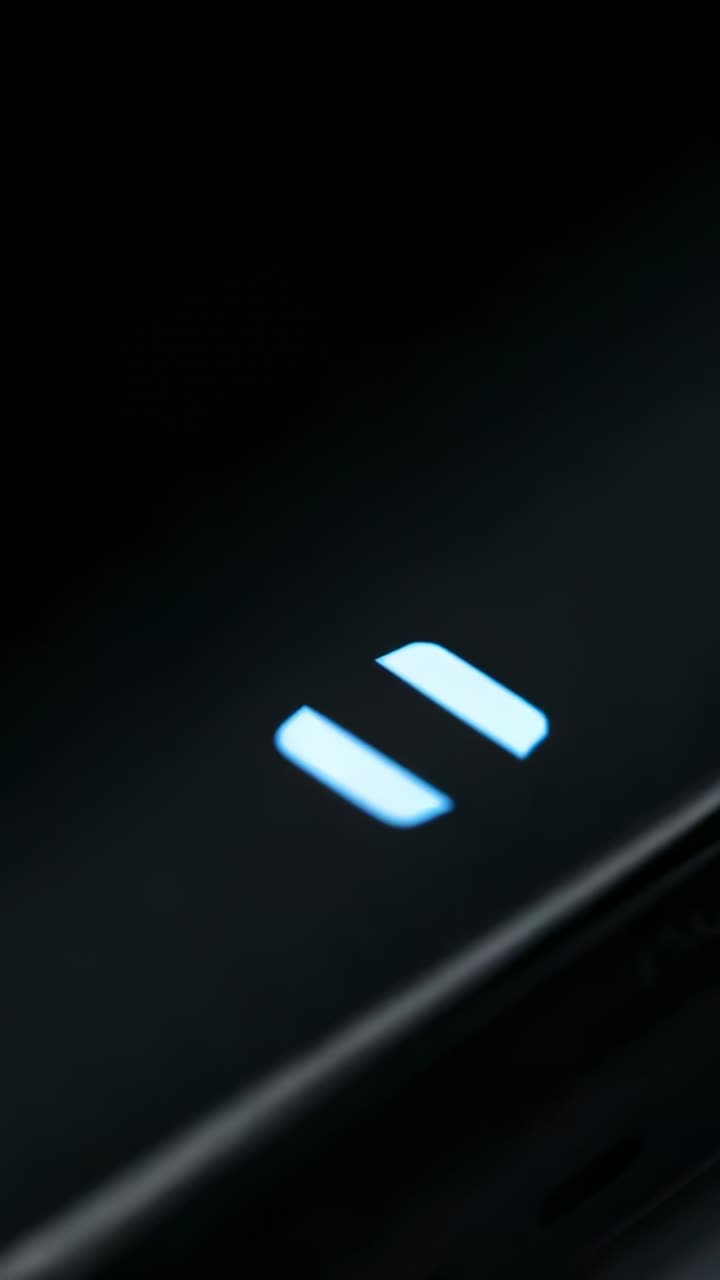 Vertical video: Shifting camera centering on lit pause icon on glossy edge, revealing port glow