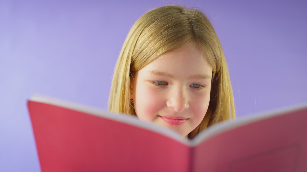 Scatto in studio di giovane ragazza che studia un quaderno scolastico su sfondo viola