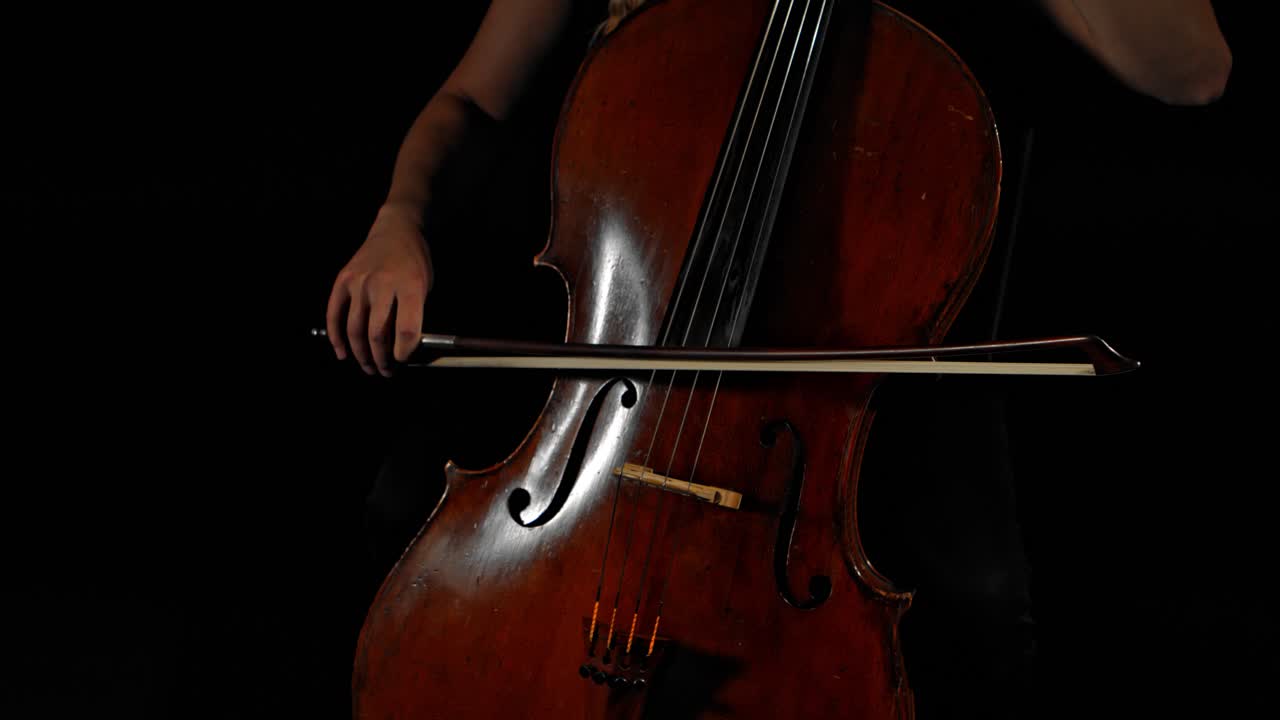 Closeup of female hands playing cello, black moody background